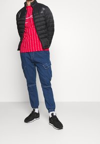 Svart puffjacka, röd tie-dye t-shirt, blå cargobyxor, svarta sneakers. Strukturerat tyg med en åtsittande siluett och fickor på byxorna.