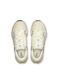 Chaussures de sport de couleur crème avec une tige en maille, un design texturé, une semelle rembourrée et des détails de logo. Elles disposent de lacets plats et d'un bout rond.