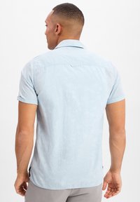Himmelblaues Kurzarmhemd aus einem Stoff mit feinem Palmenblattmuster. Verfügt über einen klassischen Kragen und ein Rückenpasse-Detail.