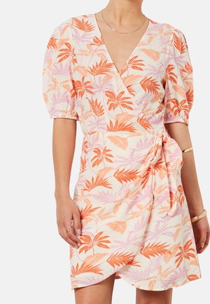 Femme portant une robe portefeuille courte avec des manches bouffantes, ornée de motifs de feuilles tropicales orange et rose sur un fond clair.