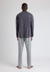 Camiseta gris de manga larga con corte recto, combinada con pantalones grises estampados que presentan un diseño intrincado; tela suave con una textura lisa.