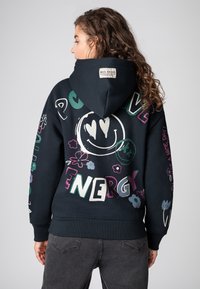 Zwarte hoodie met kleurrijke grafische ontwerpen, waaronder bloemen en een glimlachend gezicht, met teksten zoals "LIEFDE" en "ENERGIE" op de achterkant.