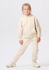 Beige hoodie met kangoeroe-pocket en bijpassende sweatpants. Zacht materiaal, ontspannen pasvorm, ribgebreide manchetten en voorzien van een klein, logo-detail.