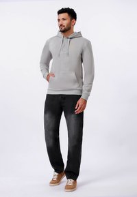 Felpa con cappuccio grigio chiaro con tasca frontale e coulisse, con un piccolo logo giallo. Abbinata a jeans grigio scuro e sneaker color cuoio.