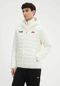 Chaqueta de plumas blanca con capucha, que presenta un parche de logo negro y un emblema colorido en el hombro. Diseño acolchado texturizado.