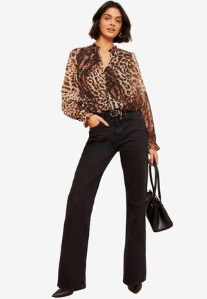 Blusa trasparente leopardata marrone con scollatura arricciata, abbinata a jeans neri a vita alta a campana. Accessoriata con una piccola borsa nera.