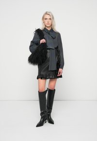 Melnas ādas svārki ar viļņotu apakšmalu, raibu krekliņu ar pogām un tauriņu, kā arī melnas uz ceļgaliem augstas papēžu zābaki. Mākslīgas ādas melna somiņa.