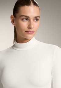 Biely rolák vyrobený z hladkého, elastického materiálu. Obsahuje priliehavý strih s vysokým golierom a bezšvový vzhľad.