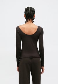 Καφέ εφαρμοστό τοπ με μακριά μανίκια και φαρδιά στρογγυλή πλάτη. Κατασκευασμένο από απαλό ύφασμα, διαθέτει άψογες ραφές και λεία υφή.