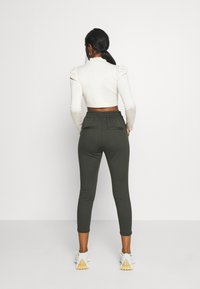 Lyhyt valkoinen paita puffihihnoilla, yhdistetty tummanvihreisiin istuviin verkkareihin, joissa on takataskut, ja valkoisiin urheilujalkineisiin, joissa on kuvioidut pohjat.