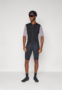 Maillot de cyclisme noir avec manches courtes en mesh, fermeture éclair à l'avant et accents réfléchissants. Associé à un short noir rembourré et des chaussures de cyclisme.
