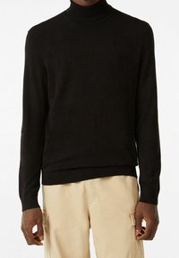 Svart polotröja i mjukt tyg, med långa ärmar, ribbade muddar och nederkant, bärs med ljusbeige cargobyxor.