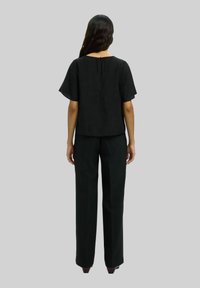 Schwarzes Oberteil mit kurzen, schwingenden Ärmeln und Rundhalsausschnitt, kombiniert mit weit geschnittenen, schwarzen Hosen. Glatte Textur, minimalistisches Design, Rückansicht gezeigt.