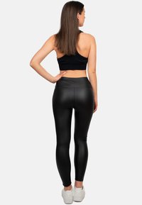 Leggings neri a vita alta con una finitura lucida e testurizzata, abbinati a un crop top nero, indossati con scarpe da ginnastica bianche.