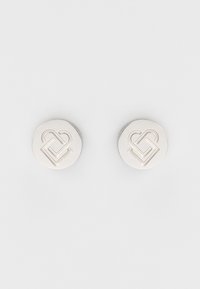 Orecchini circolari in tonalità argento con un design a cuore intrecciato in rilievo, texture liscia e finitura lucida.