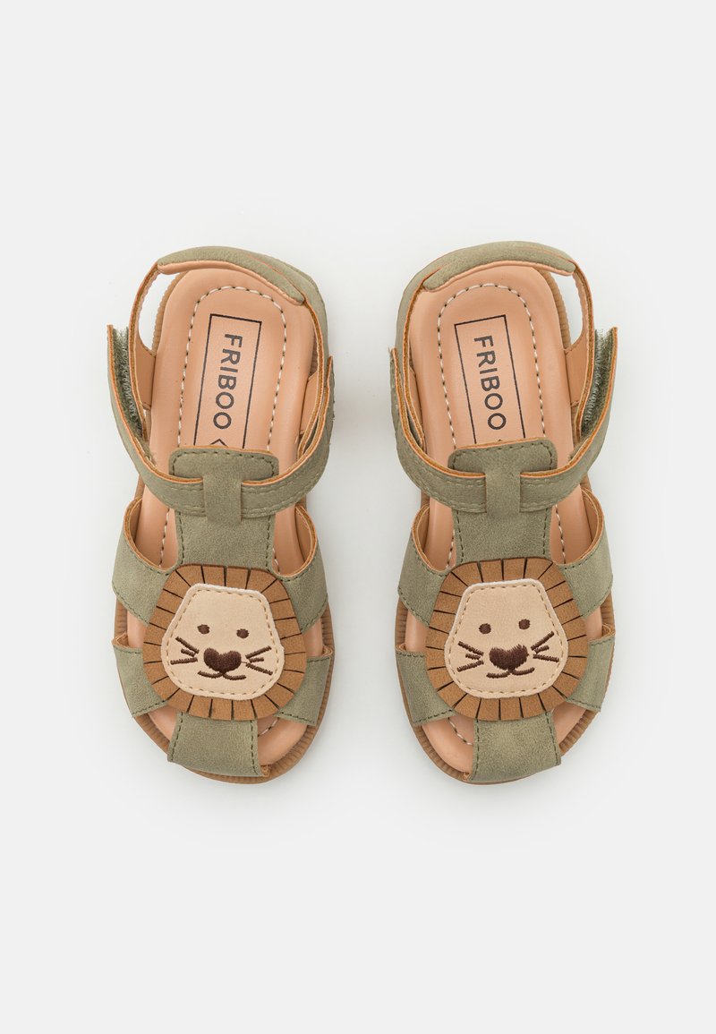 Grønne semskede sandaler med et løveansigt design på tåen, med en beige accent. Lukket bag, åbne sider og justerbare stropper.