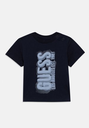 Camiseta de bebé azul marino con mangas cortas y botones a presión en los hombros, con un diseño de texto grande y vertical que dice "GUESS Los Angeles 1981" en la parte delantera.