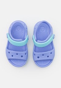 Purple rubber clogs with a light blue strap, featuring ventilation holes and a textured sole for grip. Smooth, flexible material.