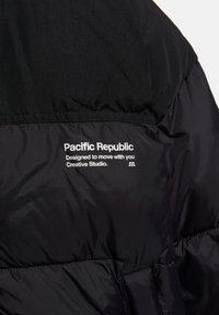Giacca nera imbottita con una superficie liscia, caratterizzata da un logo bianco e testo sul retro: "Pacific Republic Progettata per muoversi con te."