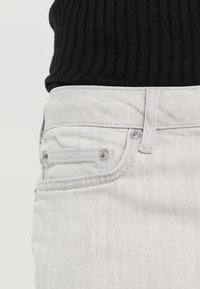 Vaaleanharmaat farkut, joissa on teksturoitu viimeistely, tavallinen viiden taskun malli ja hopeanväriset metalliosat.