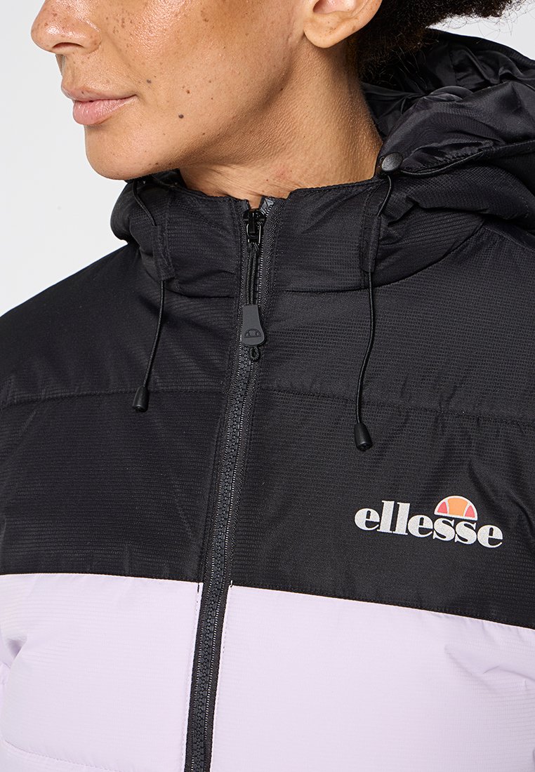 Giacca isolante nera e lilla chiaro con chiusura a zip, cappuccio regolabile e logo sul petto. Presenta una texture liscia e un design sportivo.