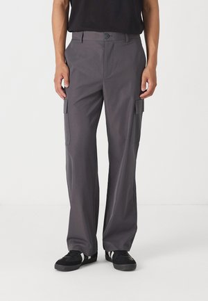 Graue Cargo-Hosen mit taillierter Passform, zwei Seitentaschen und glatter Textur. Kombiniert mit schwarzen Sneakers für einen Kontrast.