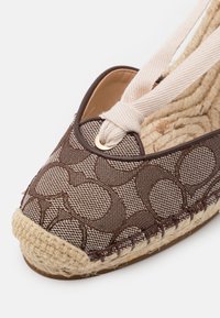 Espadrille à motif brun avec une semelle en jute tressé, dotée d'un dessus en tissu doux et de liens en tissu couleur crème pour le maintien.