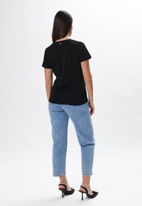 Camiseta negra de manga corta con escote redondeado, que presenta un pequeño logo en la parte posterior, combinada con unos pantalones vaqueros de cintura alta en azul claro.