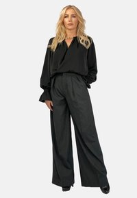 Czarna bluzka z głębokim dekoltem w kształcie litery V i bufiastymi rękawami, w połączeniu z wysokim stanem ciemnych spodni w prążki i czarnymi szpilkami. Złoty łańcuch jako akcent.