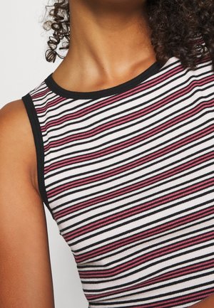 Vrouw draagt een mouwloze, geribbelde cropped top met zwarte, witte en roze horizontale strepen en zwarte biezen rond de halslijn en armsgaten.