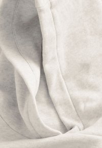 Hellgrauer Sweatshirtstoff mit weicher Textur, ausgestattet mit einer Kapuze und sichtbaren Nähten, locker drapiert in Falten.