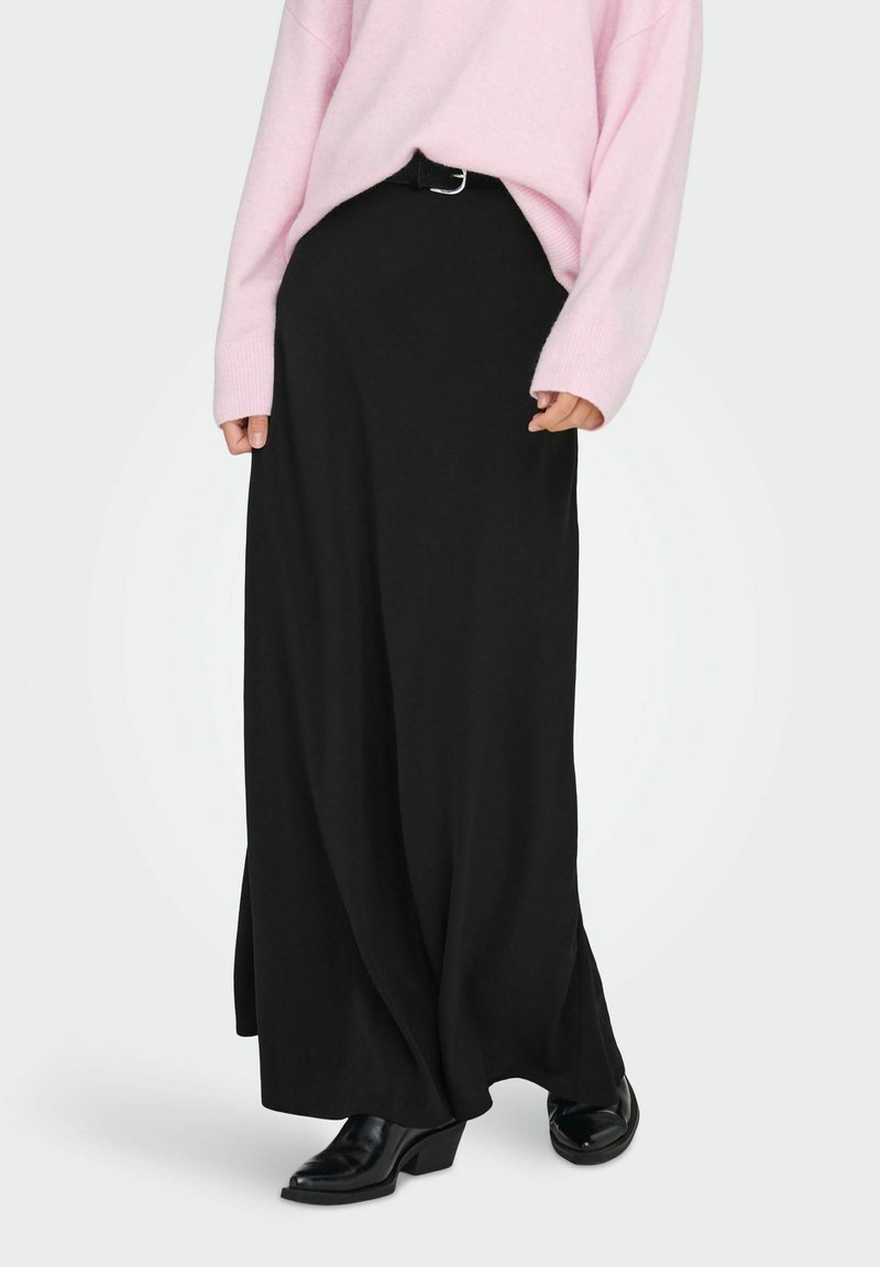 Μαύρη μακριά φούστα με ρέουσα σχεδίαση, διαθέτει ζώνη και θηλιές ζώνης. Συνδυάζεται με ροζ oversized πουλόβερ και μαύρες μπότες με τακούνι.