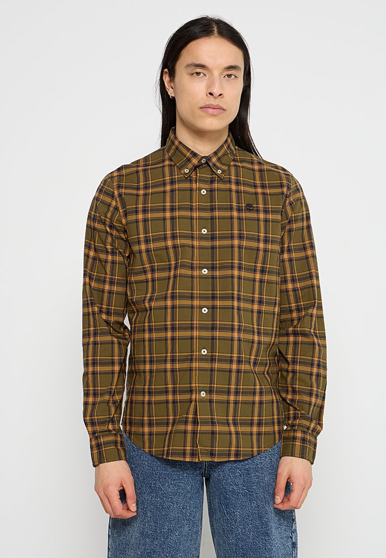 Camicia a quadri verde e marrone con bottoni bianchi, dotata di un piccolo logo sul petto e di un colletto classico. Maniche lunghe, vestibilità rilassata.