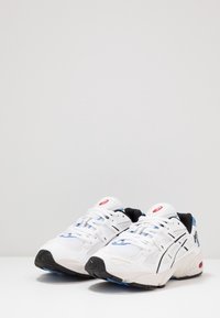 Vita sportskor i vitt med en nätövre, svarta och blå accenter, syntetiska överdrag och en gummisula med gelkuddar.