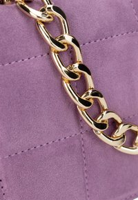 Borsa a tracolla in suede viola con una catena metallica dorata. Il corpo ha una texture trapuntata con dettagli di cucitura visibili.