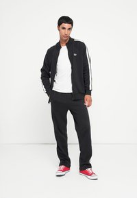 Black zip-up jacket with white side stripes, paired with a white t-shirt and black sweatpants. Red sneakers complete the outfit.
