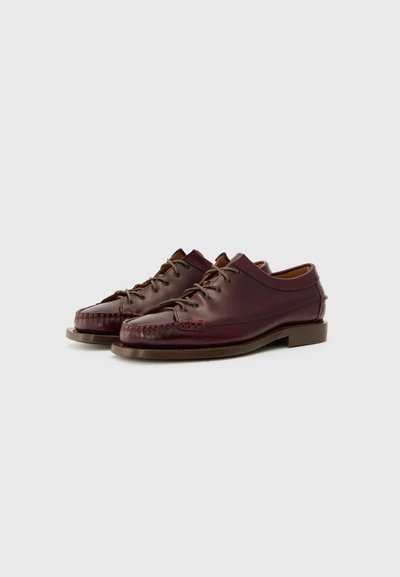 Scarpe in pelle bordeaux con punta arrotondata, cuciture intricate, stringate e con una suola bassa. Finitura liscia con dettagli di texture sottili.