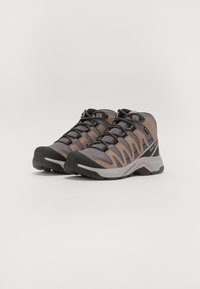 Chaussures de randonnée mi-hautes avec une tige en mesh gris et beige, capuchon en caoutchouc noir, et lacets texturés. Durables, conçues pour les activités de plein air.
