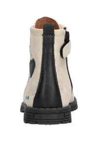 Botín de ante beige con detalles en cuero negro, diseño de corazón, cremallera lateral y suela texturizada. Presenta puntos verdes en la parte trasera.