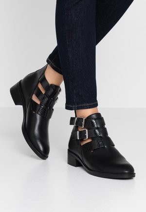 Bottines noires en cuir lisse et texturé, avec trois fermetures à sangle, des boucles en argent et un petit talon carrée.