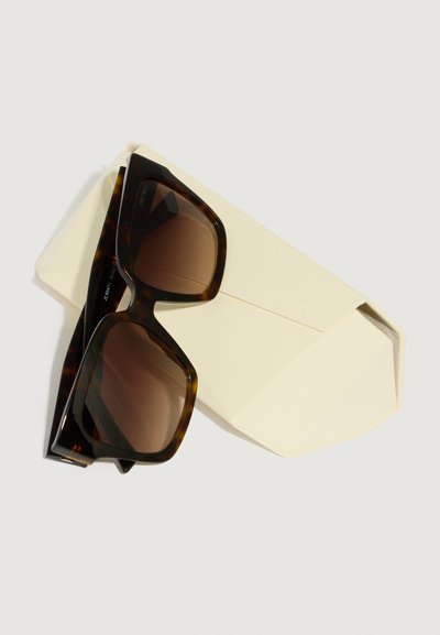 Lunettes de soleil en écaille de tortue avec des verres bruns dégradés, de forme rectangulaire, et une finition brillante. Accompagnées d'un étui doux de couleur crème.