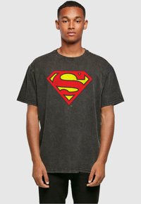 Camiseta de algodón negra con mangas cortas, que presenta un gran logo de Superman en amarillo y rojo en el frente, y un cuello redondo.