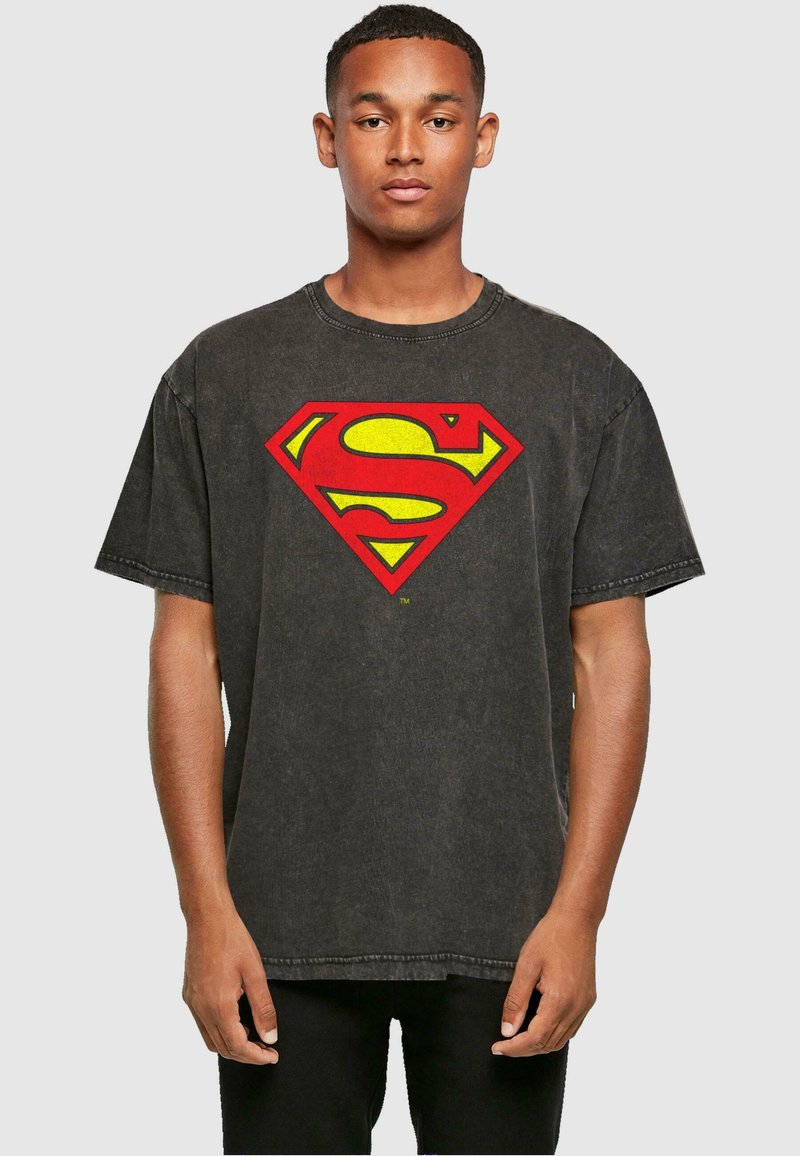 Camiseta de algodón negra con mangas cortas, que presenta un gran logo de Superman en amarillo y rojo en el frente, y un cuello redondo.