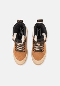 Chaussures en daim marron et crème avec des lacets noirs, une semelle en caoutchouc texturée et une doublure en polaire. Vue de dessus montrant les détails du design et du logo.