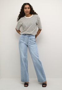 Striped short-sleeve shirt in cream and black, paired with light blue wide-leg jeans. Smooth fabric with a relaxed fit. Square-toed black sandals.