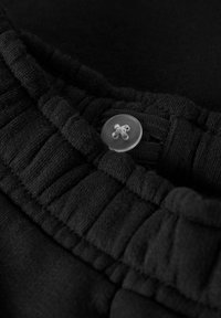 Zwarte stof met ribbelstructuur, met een doorzichtige knoop met een kruisontwerp. Close-up van de tailleband en sluitdetails van het kledingstuk.