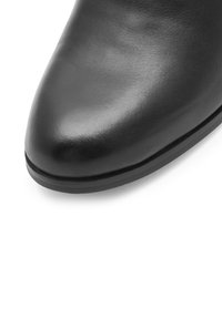 Čierna kožená členková topánka s špicatou špičkou a hladkou textúrou. Obsahuje tenkú čiernu podrážku a minimalistický dizajn bez ozdôb.
