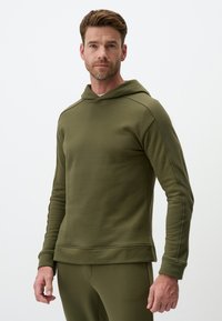 Hoodie verde oliva in un tessuto morbido, con tasca frontale, cappuccio foderato e polsini e orlo a coste, abbinato a pantaloni coordinati.