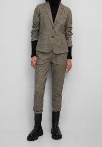 Grå texturerad blazer med två knappar och fickor, i kombination med matchande tajta byxor. Svarta knä-höga stövlar fulländar outfiten.