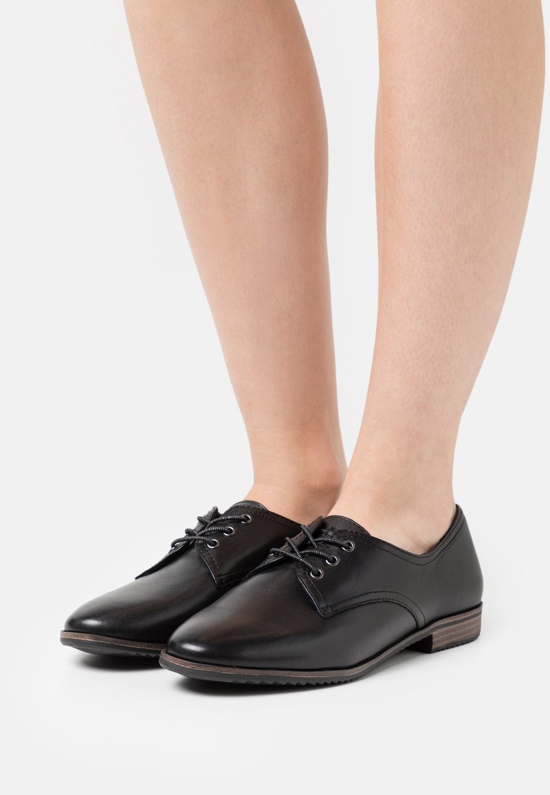 Chaussures en cuir noir à lacets, avec un bout arrondi, une tige texturée et un petit talon en bois, présentant des coutures minimales et une finition lisse.